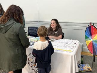 Librarian sits at East Providence Public Library activity table talking to a parent and child
