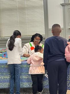 Author Oge Mora sitting at a table signing books for children